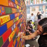 Woman painting a brick on a wall with other people painting in the background