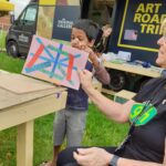 a small boy shows off his painting in front of the National Gallery Road Trip sign