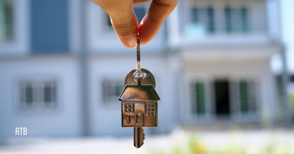 image of hand holding set of house keys with a row of houses in the background